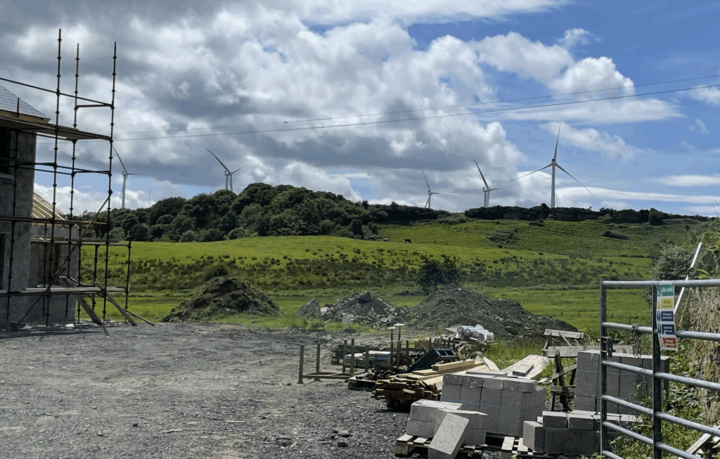 Wind turbines affect the view as they tower over a horse field/hill behind a construction site.